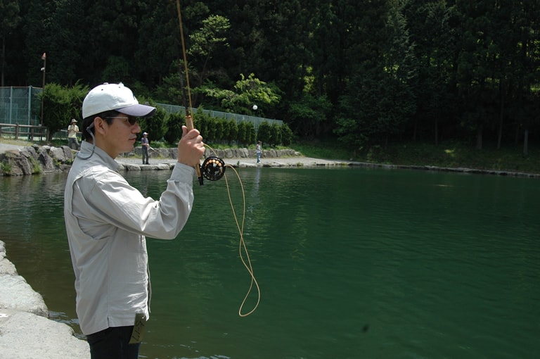 ラインを後方にキャストする。この時はロッドを持った手を上空に撥ね上げ、最終的にロッドを持つ手を顔の横で止める。この動きをピックアップという。